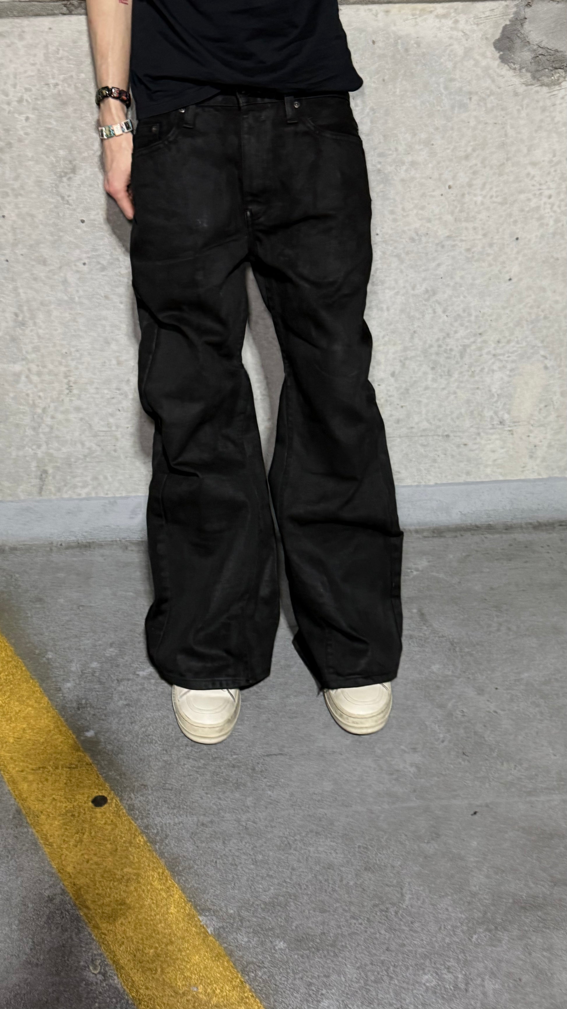 Waxed flared denim jeans by WithoutSaint, showing the dark, shiny fabric and high-waisted fit with flared leg style.